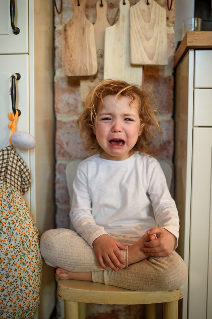 Portrait of unhappy small girl sitting indoors in kitchen at home, crying